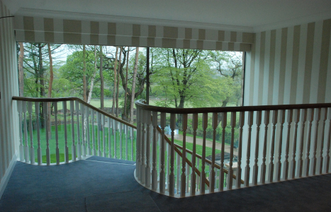 A landing view of the start of a stair case, with a window view of a garden.