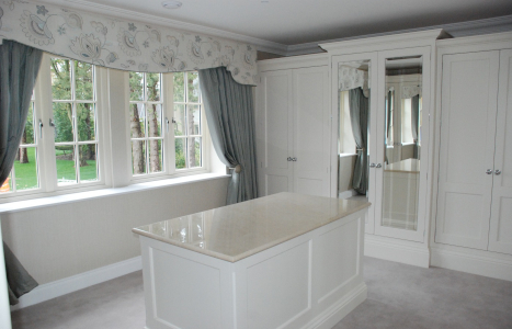 A light white and grey walk in dressing room containing an island and wardrobes, where two doors are mirrored.